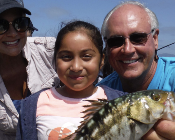 Young girl with a big smile holding a pretty big fish! Next to two smiling adults.